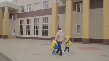 Kızlar okul çantalarıyla okula giderken babalarının elini tutarlar, küçük çocuklar için eğitim programı, çocuk ve baba için acele sınıfı, anaokulu eğitimi, okul öğrencileriyle ilgilenmek, mutlu aile hayatı.