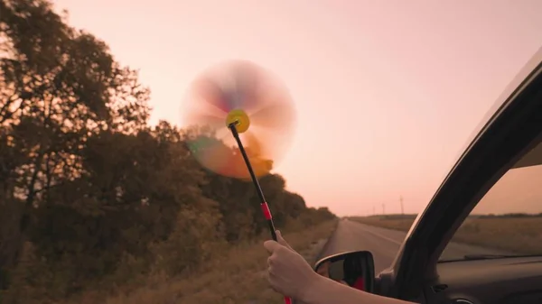 Chica libre agitando un molinete fuera de la ventana del coche en el viento, viaje camino de aventura al atardecer rosa, paseo en coche familiar, llegar por la ventana del coche a la luz del sol del cielo, disfrutar del movimiento, concepto de sueño de la infancia —  Fotos de Stock