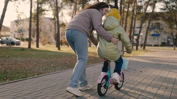 Мама вчить маленьку дитину їздити на велосипеді в місті, дитина їде на тротуарі, щаслива сім'я, дитина грає і сміється з мамою, вчиться їздити, змушує дитинство мріяти справжні дівчата, дочка і мама смішні — стокове фото