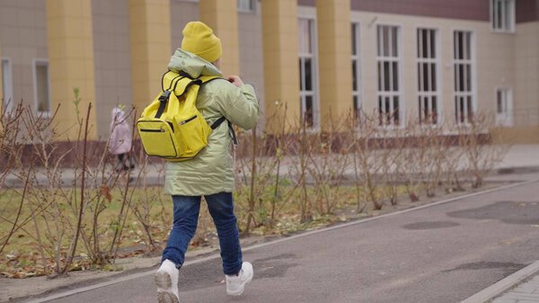 little child through schoolyard to school with a backpack, happy kid rushes runs to lesson in class, concept of school development of childhood, concept of elementary initial development of students