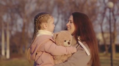 Anne kucağında bir ayı, mutlu bir aile, parkta annesiyle yürüyen küçük bir çocuk, sonbaharda şehir parkında aile yürüyüşü, oyuncak ayı çocukların en sevdiği çocukluk oyuncağı.