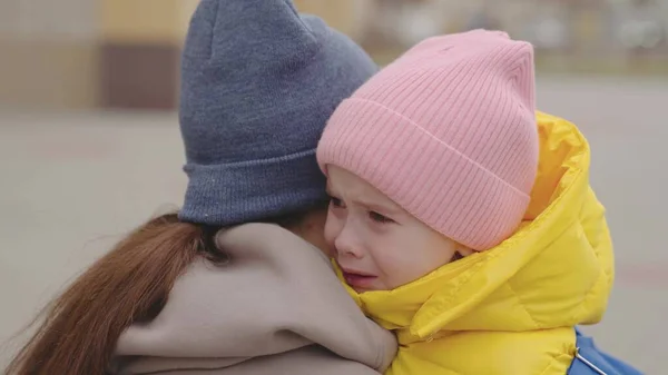 Malé dítě pláče na rameni matka, matka objímá vrtošivé dítě dívka, dcera špatná nálada, dítě ukazuje svou nelibost rodiče s hysterií, close-up, dítě výraz emoce se slzami, smutný obličej — Stock fotografie