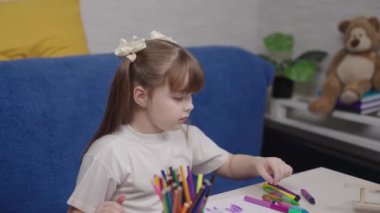 Küçük kız pastel boyalarla parlak renkli resimler çiziyor, boya kalemleriyle çocuk sanatı, çocuk aklının yaratıcı hayal gücü, hafta sonları açık hava aktiviteleri, bebek güzel bir albüm çizmeyi öğreniyor.