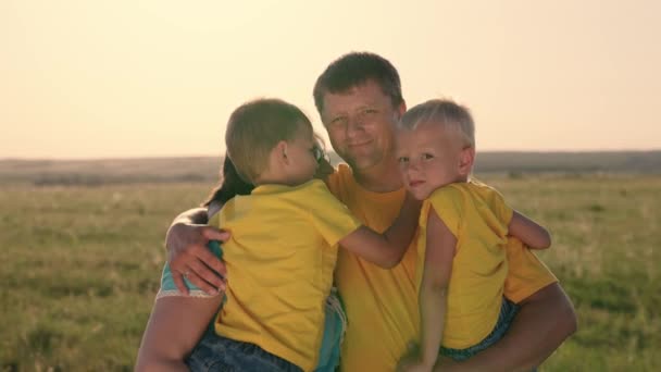 Father farmer hugs sons and wife in the field at sunset, woman with husband and kid walk in nature together and smile, love in a happy family, teamwork, business concept, weekend summer vacation — Stockvideo