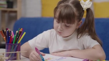 Küçük kız çizim defterinde pastel boyalarla resim çiziyor, çocuk yaratıcılığı kavramı, parlak renkli kalemlerle çizimler masasında oturuyor, ressam olmak için kavramsal bebek hayalleri, fantezi kurmak için.