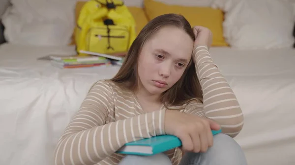 An upset girl with book her hands sits in childrens bedroom room, teenager schoolgirl is sad alone with resentment her eyes, concept good mood, negative emotions kid, neurosis at school age student — Foto Stock