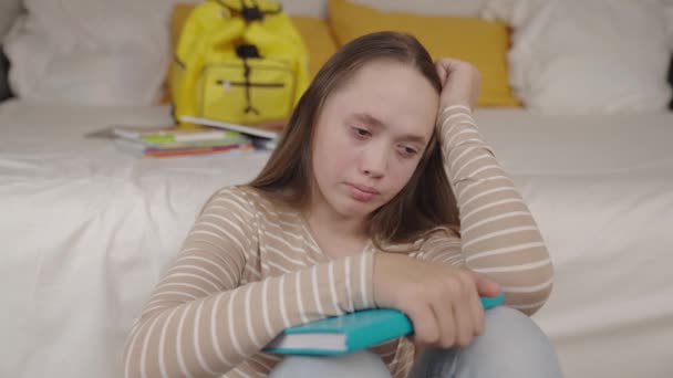 An upset girl with book her hands sits in childrens bedroom room, teenager schoolgirl is sad alone with resentment her eyes, concept good mood, negative emotions kid, neurosis at school age student — Stock Video