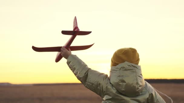 Little child runs at sunset with toy plane in his hands, happy family life, childhood dream of flying, running kid fantasizes about pilots flight, cheerful baby runner in nature travels on weekends — Video Stock