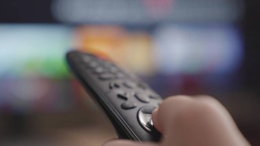 Kafkasyalı bir elin uzaktan kumandalı bir TV kanalı ile yakın çekimi, bir TV uzaktan kumandası, kanalları ve TV programlarını çevirmek, sinema uygulamasında istenen filmi aramak.