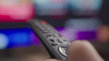 Kafkasyalı bir elin uzaktan kumandalı bir TV kanalı ile yakın çekimi, bir TV uzaktan kumandası, kanalları ve TV programlarını çevirmek, sinema uygulamasında istenen filmi aramak.