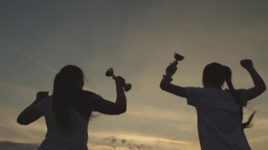 Kazanan kızların silueti altın bardaklarla mutluluktan atlıyor elleri, yarışma günbatımını kazanan sporcu kadınlar, neşeli takım çalışması gününü kutluyorlar, konsept kadın başarısı, Afrika şampiyonu