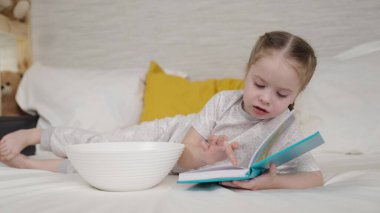 Küçük çocuk yatakta uzanmış çocuk odasında kitap okuyor, ev ödevi yapıyor birinci sınıf, ilkokul mektupları okuyor, çocuk peri masalları olan ilginç bir edebiyat kitabı okuyor.