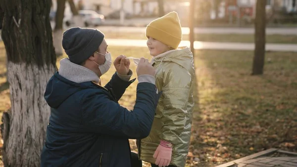 Ojciec nosi dziecięcą maskę na twarzy podczas spaceru po parku miejskim, chroni ciało dziecka przed infekcją koronawirusową, mała córka i tata przestrzegają zasad kwarantanny podczas wychodzenia, szczęśliwa rodzina — Zdjęcie stockowe