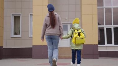 Anne, okul çantalı küçük çocuğu okula götürüyor, çocuk, ilkokul öğrencisi sınıfa gitmek için acele ediyor, ilkokul çocuğu eğitimi, çanta taşıyan kız, annesini elinden tutuyor.