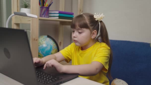 Little child does homework on a laptop, a girl types on a keyboard, home school on a computer online, learning a kid remotely at home, playing games in computer application program, modern technology — Wideo stockowe