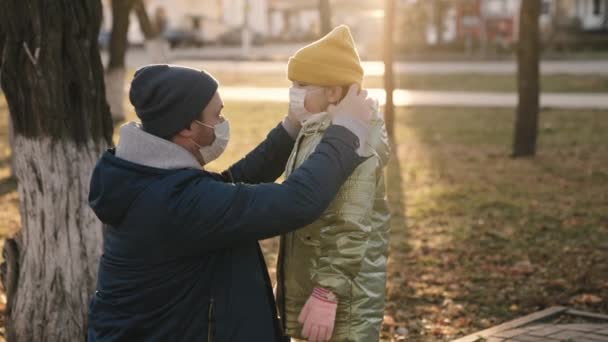 Padre lleva máscara de niño en su cara mientras camina por el parque de la ciudad, proteger el cuerpo de los niños de la infección por coronavirus, hija pequeña y papá cumplen con las reglas de seguridad de cuarentena para salir, familia feliz — Vídeos de Stock