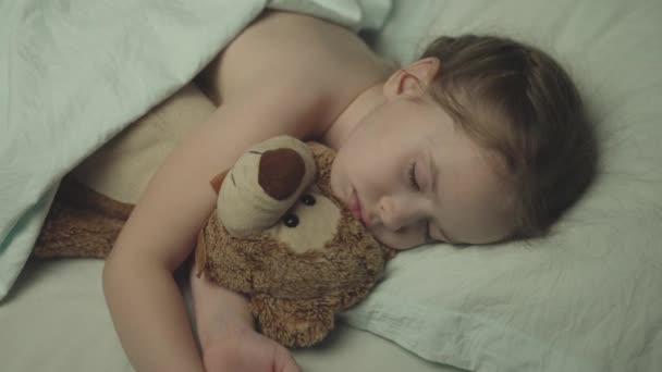 Little baby sleeps at night in crib an embrace with teddy bear, girl daughter dreams while lying bed with her eyes closed, child with friend with doll bear rest together, kid face and toys close-up — Vídeo de Stock