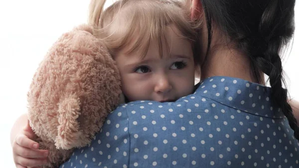 一位母亲用泰迪熊安抚了抱着和摇动着泰迪熊的小孩，一位心烦意乱的小孩在母亲的怀抱中寻求支持，一个家庭关系的概念，一位女保姆则是这样看待的 — 图库照片