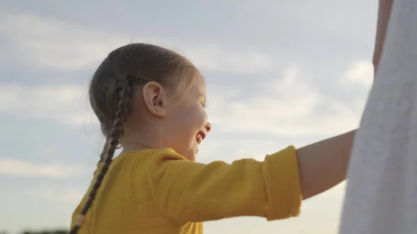 Niña sostiene a sus madres de la mano y se ríe al atardecer la luz del sol, hija con su amada madre están caminando juntos sonriendo, familia feliz, niño alegre viaja la naturaleza, niño en aspectos destacados brillantes — Foto de Stock