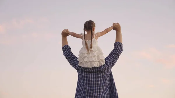 Concept father and daughter, happy family life, walk dad and child sitting on shoulders astride nature, happy child ride dad, persons play fun game together, little kid dreams of flying, being pilot — Photo