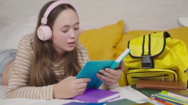 Genç bir kız kanepede uzanıp kitap okuyor, bir çocuk kulaklıkla müzik dinliyor, modern bir çocuk okul edebiyatı okuyor, öğrencilerin gençlik eğitimi alıyor, kitap sayfalarıyla bilgi kazanıyor.