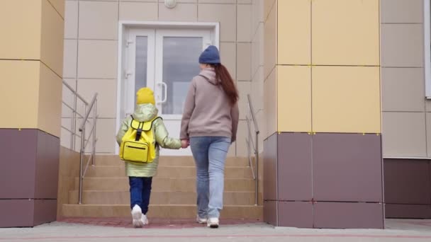 Маленька дитина з рюкзаком йде зі своєю матір'ю в руках до школи. концепція освіти дітей. маленька дитина і мама поспішають до уроку разом. щаслива сім'я разом. студентська рука з матір'ю — стокове відео