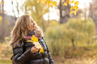 Sarı akçaağaç yaprakları dökülen genç bir kadın bir sonbahar parkında ellerini bırakıyor..