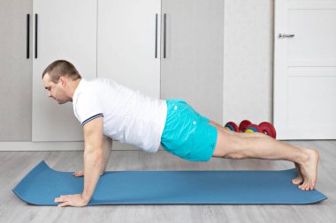 Güçlü, kaslı, kalas pozisyonunda antrenman yapan sağlıklı bir adam. Evde fitness