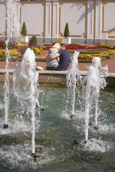 一对年轻夫妇正坐在喷泉边 男孩和女孩正在互相拥抱 — 图库照片