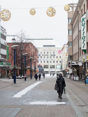 Bir kadın Noel alışverişiyle karlı caddede yürüyor. Öte yandan çanta Marimekko 'dan ve bir çanta dolusu tuvalet kağıdı var..