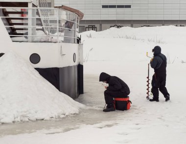 İki adam buzda buzda balık tutuyor. Hemen yanlarında bir tekne var ama dışarıda balık tutmayı tercih ediyorlar..
