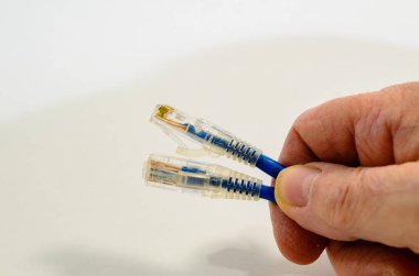 Beyaz bir arkaplana karşı iki mavi ağ kablosu tutan bir adamın yakın plan görüntüsü.
