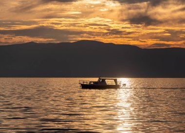 Küçük turist teknesi gün batımında bir gölde yelken açar.