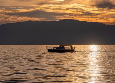 Küçük turist teknesi gün batımında bir gölde yelken açar.