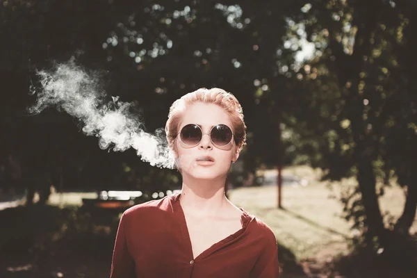 吸烟在院子里的眼镜的年轻女子 — 图库照片