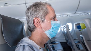 Side view of a middle aged man wearing a face mask sitting in an empty airplane