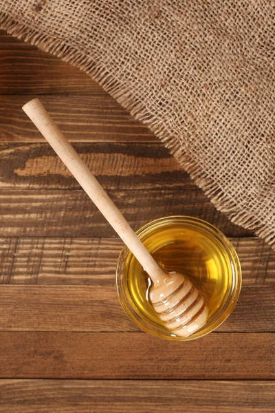 Miel en un recipiente de vidrio sobre un fondo de tablas de madera — Foto de Stock