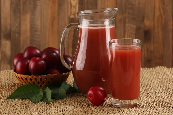 Plum juice in a glass and pitcher, plums in a wicker basket — Stock Photo, Image