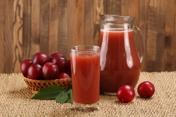 Plum juice in a glass and pitcher, plums in a wicker basket on a — Stock Photo, Image