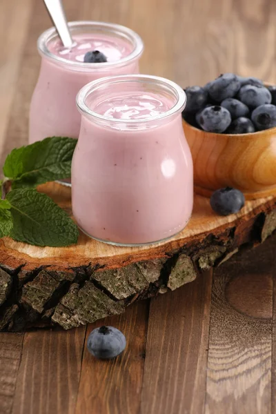 Yogurt with blueberries in a glass jar and blueberries in a wood — Stock Photo, Image