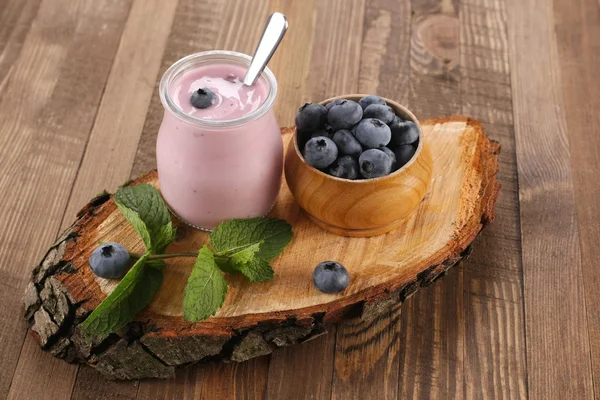 Iogurte com mirtilos em um jarro de vidro e mirtilos em uma madeira — Fotografia de Stock