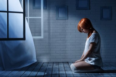 Lonely girl sits in an empty dark room clipart