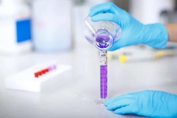 Decanting a violet liquid into a graduated cylinder — Stock Photo, Image