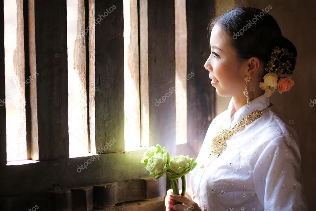 Thai girl hold lotus flower stand next to window in temple