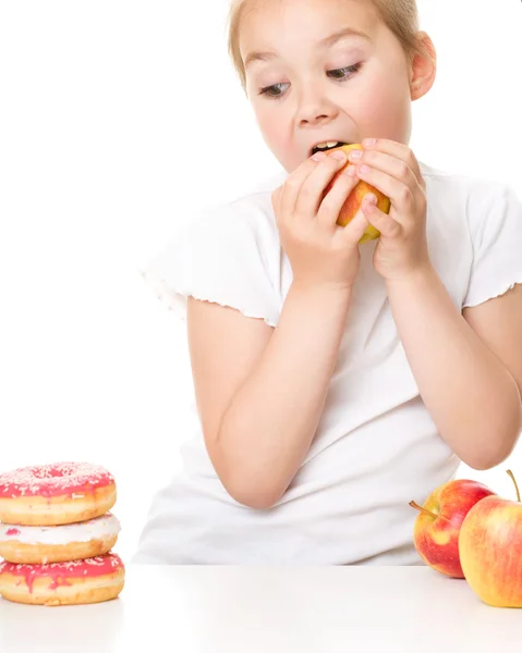 Cute girl choosing between apples and cake — Stock Photo, Image