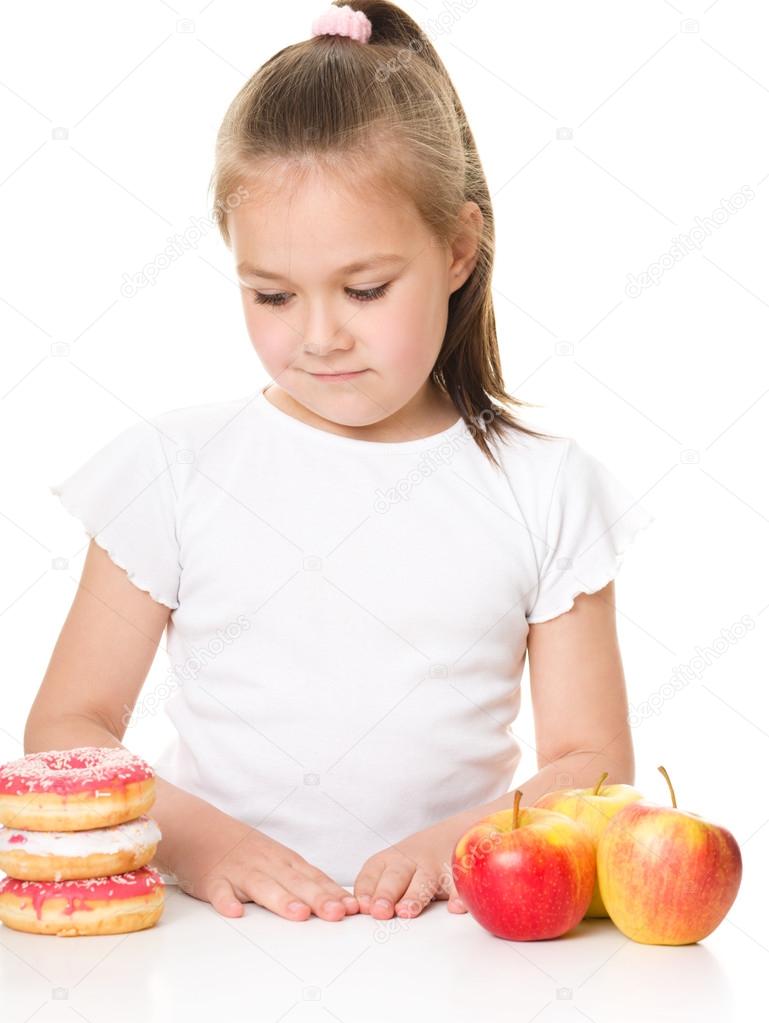 Cute girl choosing between apples and cake — Stock Photo © julaszka