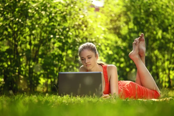 Jeune femme avec ordinateur portable sur herbe verte au parc — Photo