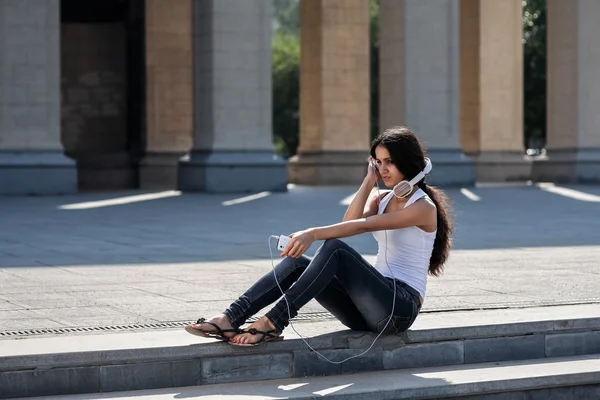 Молодая женщина сидит на лестнице, рядом с университетом, слушать — стоковое фото