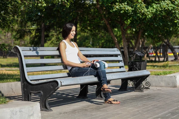Молодая женщина сидит на скамейке, рядом с университетом, слушает — стоковое фото
