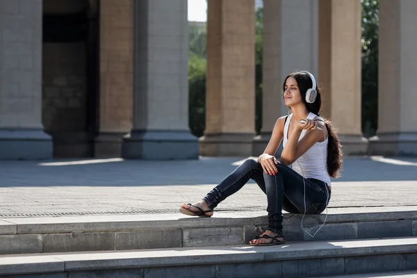 A young woman sitting on the stairs, near the university, listen — Stock Photo, Image